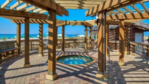 Um deck de madeira com piscina, pérgulas de madeira e vista para a praia.