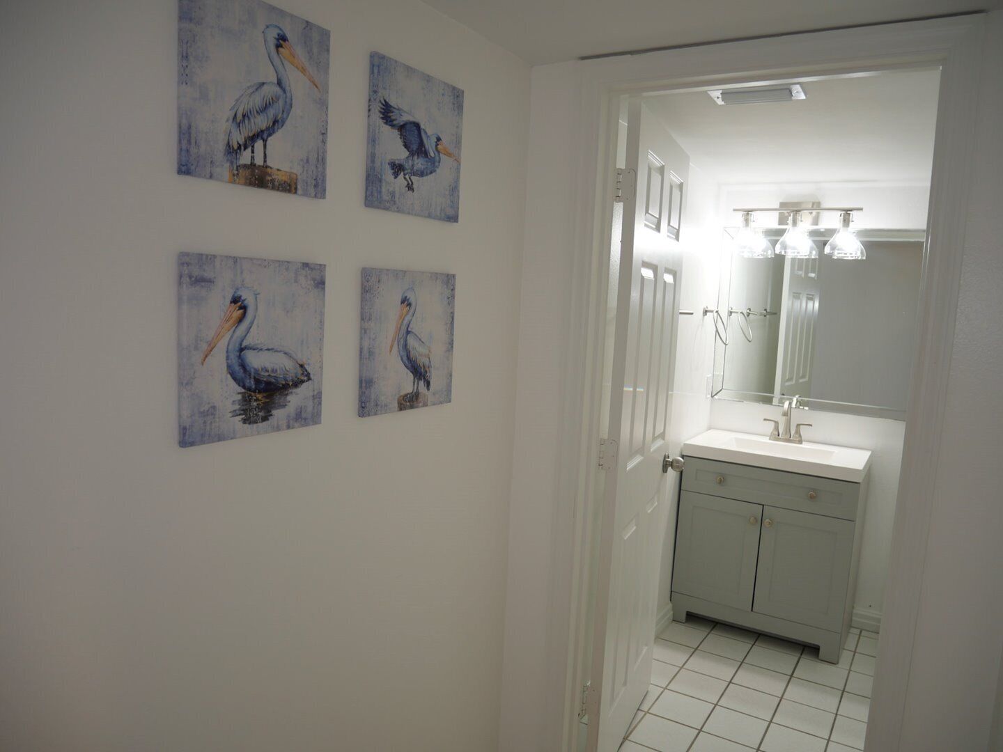 A bathroom with a white sink, a mirror, and four wall-mounted paintings of pelicans.