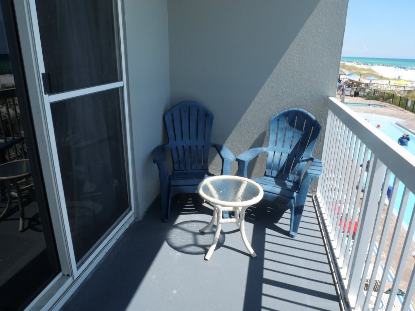 A balcony with two blue Adirondack chairs and a small white table.