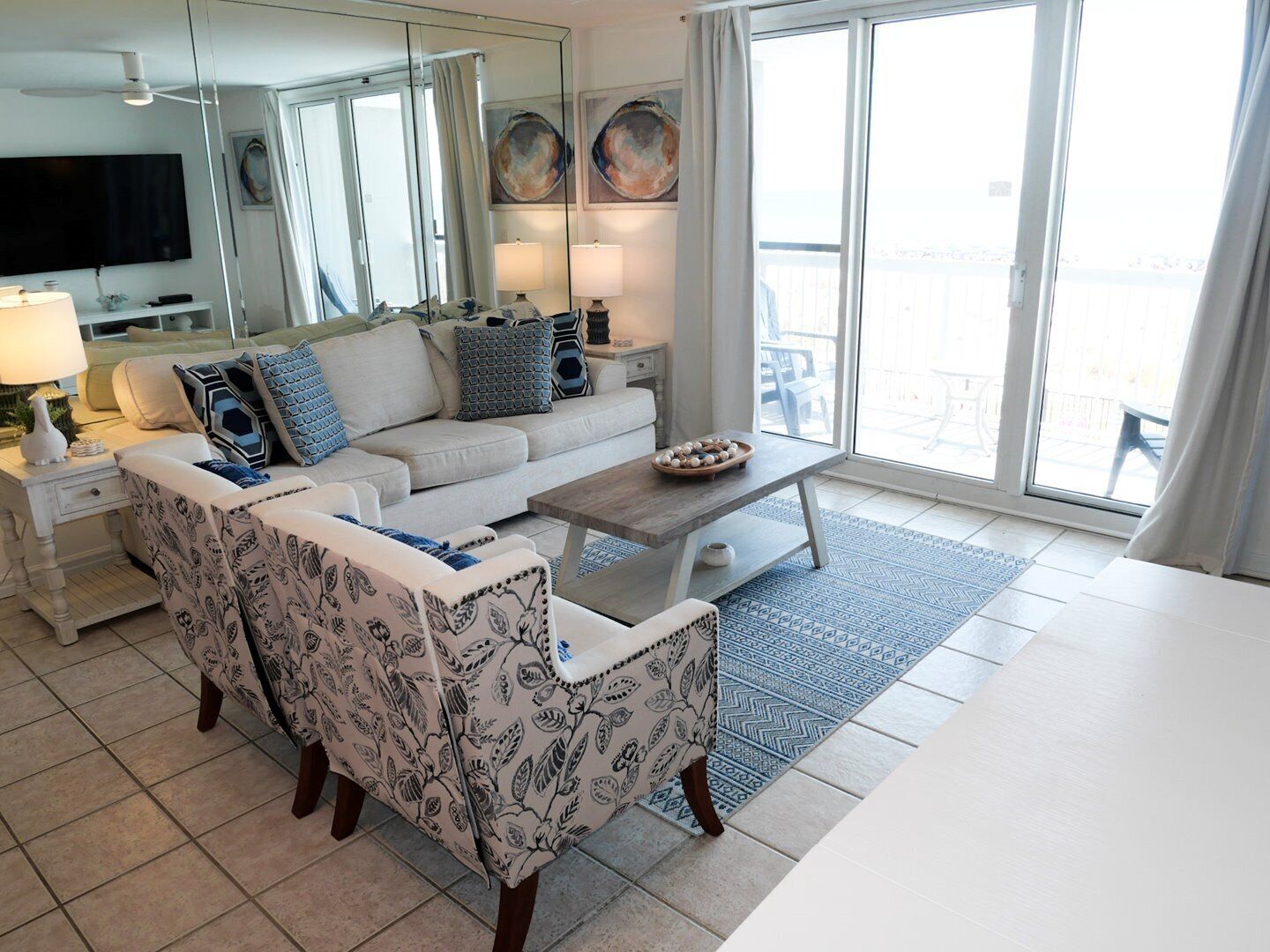 Uma sala de estar moderna com sofá, poltrona, mesa de centro e televisão. Há uma varanda com vista.