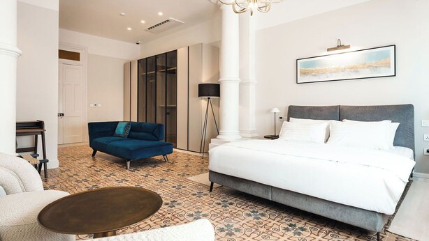 Une chambre d’hôtel moderne avec un grand lit, un canapé bleu, une petite table ronde et un sol à motifs.