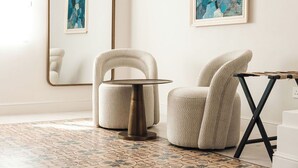 Une pièce moderne avec une table ronde, un fauteuil rembourré, un miroir et une œuvre d’art abstraite au mur.