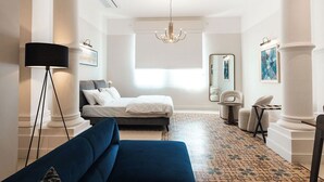 Une chambre d’hôtel avec un lit, un canapé bleu, un bureau, une chaise, une lampe sur pied et un lustre.