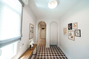 A hallway with a patterned floor, framed artwork on the walls, a bench with flowers, and a door at the end.