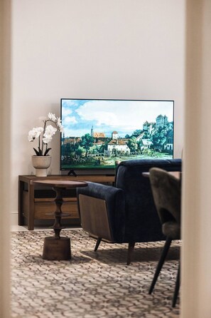 Olohuoneessa on taulutelevisio, ruukkuorvidea, puinen sohvapöytä ja tummansininen sohva.