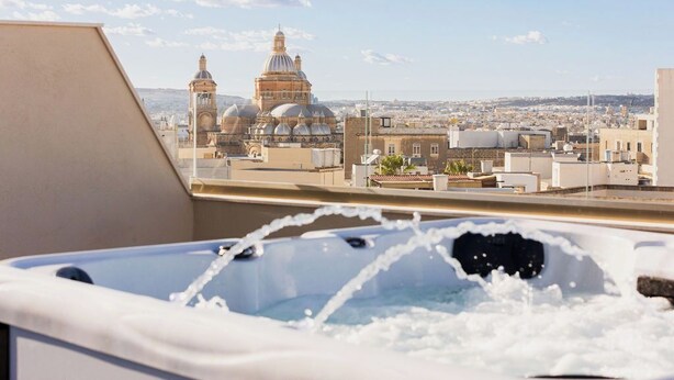 Un bain à remous avec jets d’eau, une vue sur un paysage urbain avec des bâtiments à coupoles et un ciel dégagé.