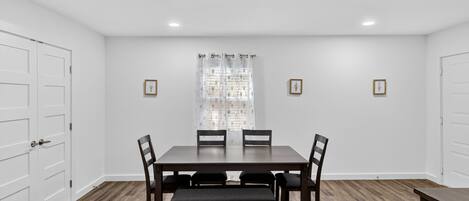 A dining room with a rectangular table, six chairs, a bench, and a window with a floral curtain.