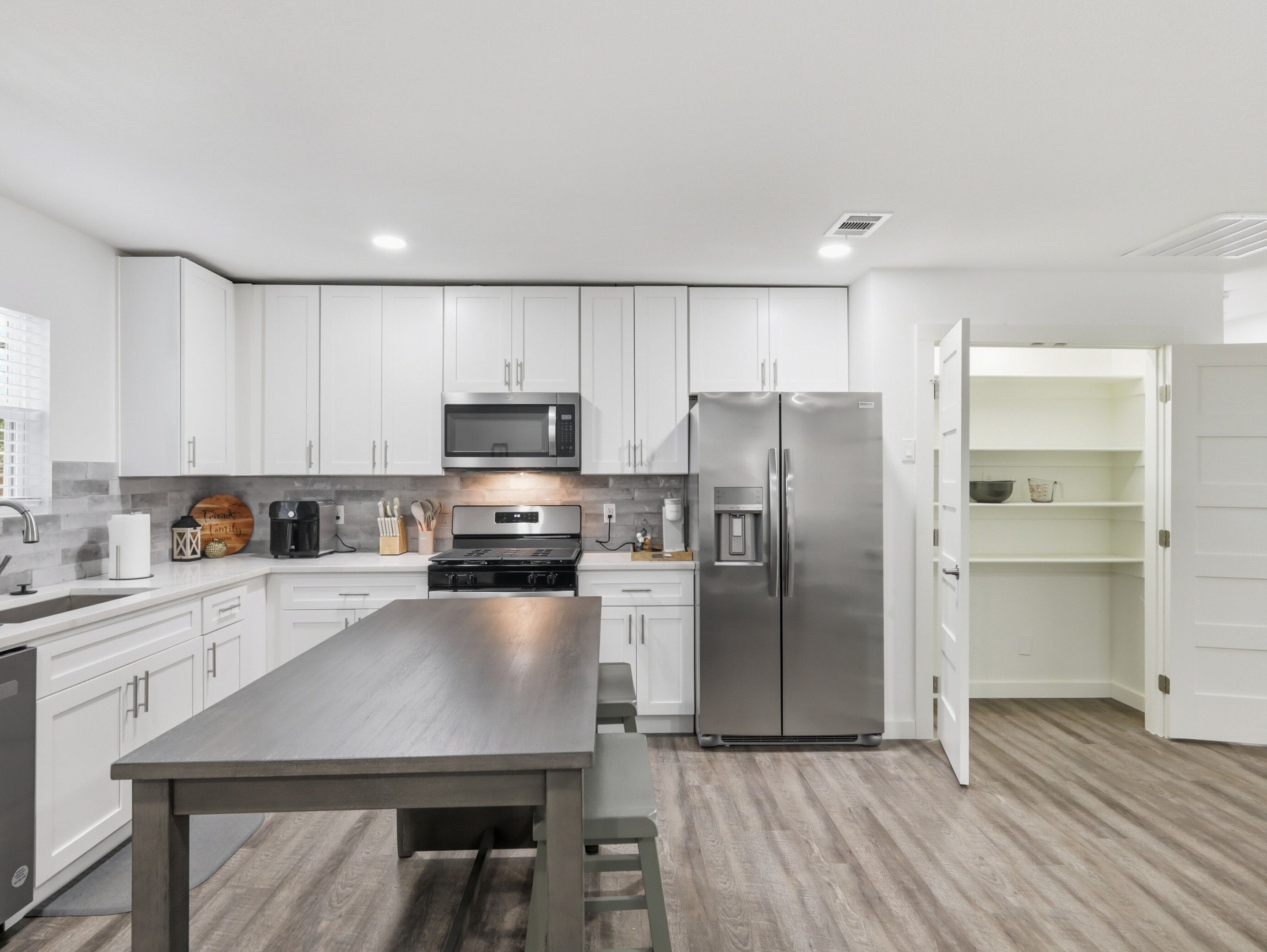 A modern kitchen with white cabinets, stainless steel appliances, and a wooden table.
