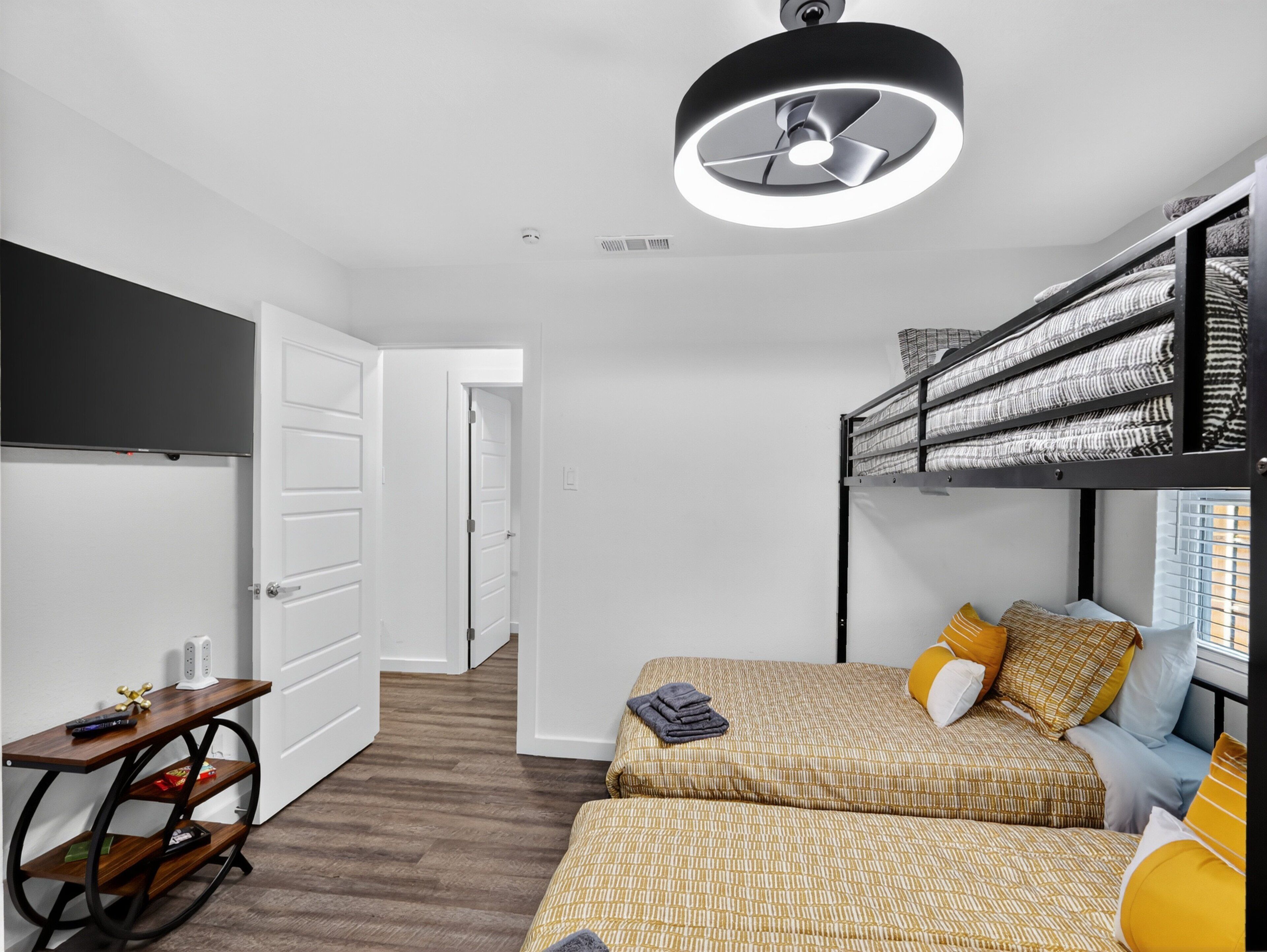 Une petite pièce avec des lits superposés, un bureau avec une chaise et un ventilateur de plafond.