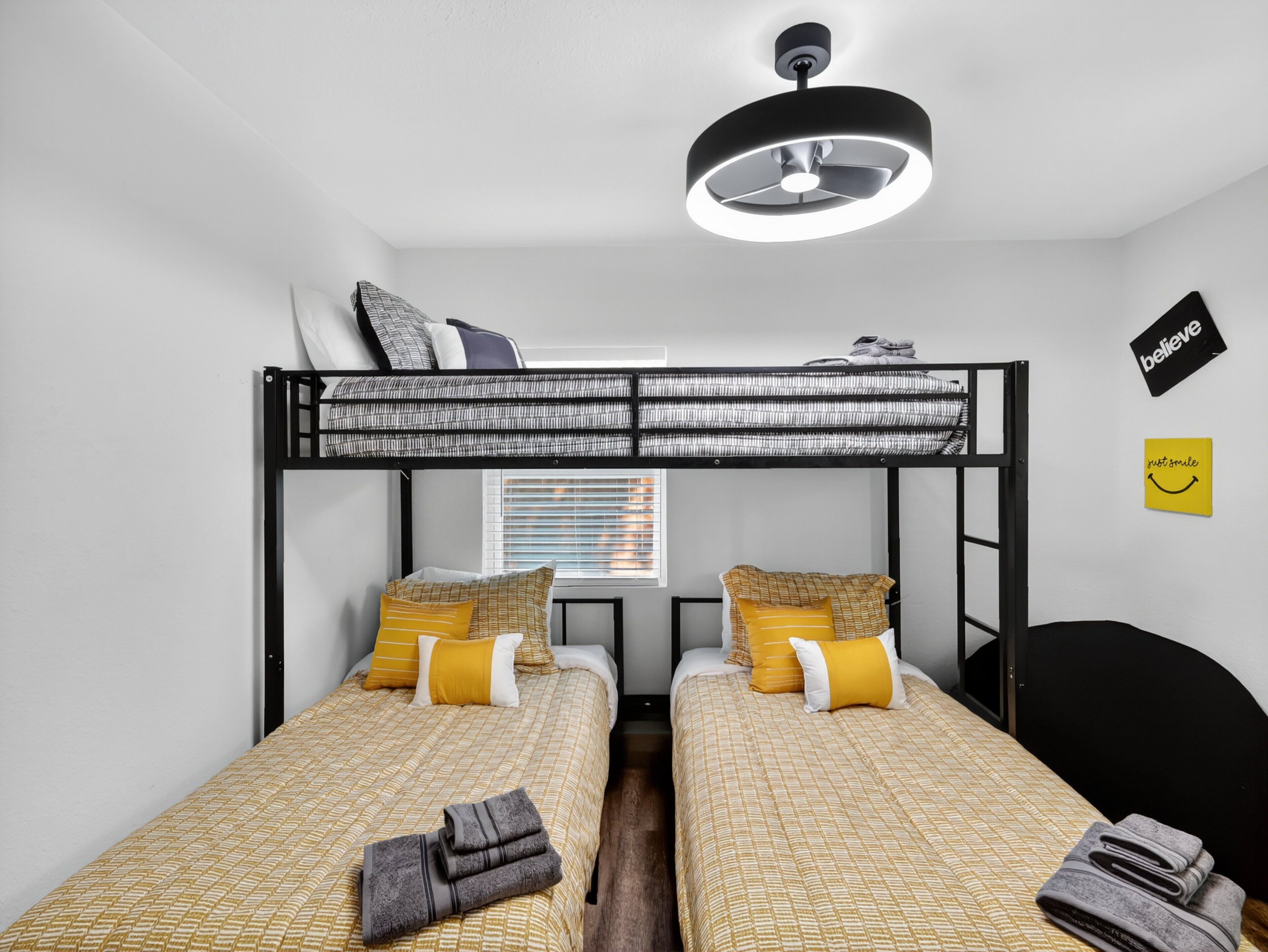 A bunk bed room with a ceiling fan, two beds with patterned bedding, a desk, and a wall with motivational stickers.