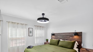 Ein ordentlich eingerichtetes Schlafzimmer mit Holz-Kopfteil, einem Bett mit grüner Bettwäsche, einem Nachttisch und einer Deckenleuchte.