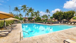 A swimming pool with lounge chairs and umbrellas, surrounded by palm trees and buildings. - Kksr#6301 Ocean/Golf Course Views, Top Floor, Corner Unit, Cathedral Ceilings (Kailua Kona)