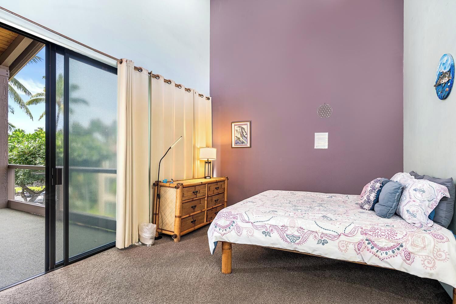 A bedroom with a bed, a nightstand, a lamp, a wall-mounted artwork, and a sliding glass door leading to a balcony.