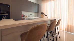 A modern kitchen with a marble countertop, a built-in oven, and a large window with sheer curtains.