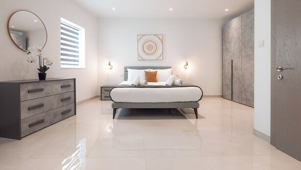 A modern bedroom with a bed, bedside tables, a dresser, a mirror, and a window with blinds.