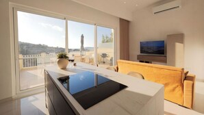 A modern kitchen with a large island, a sofa, and a TV in a living area with large windows and a balcony.