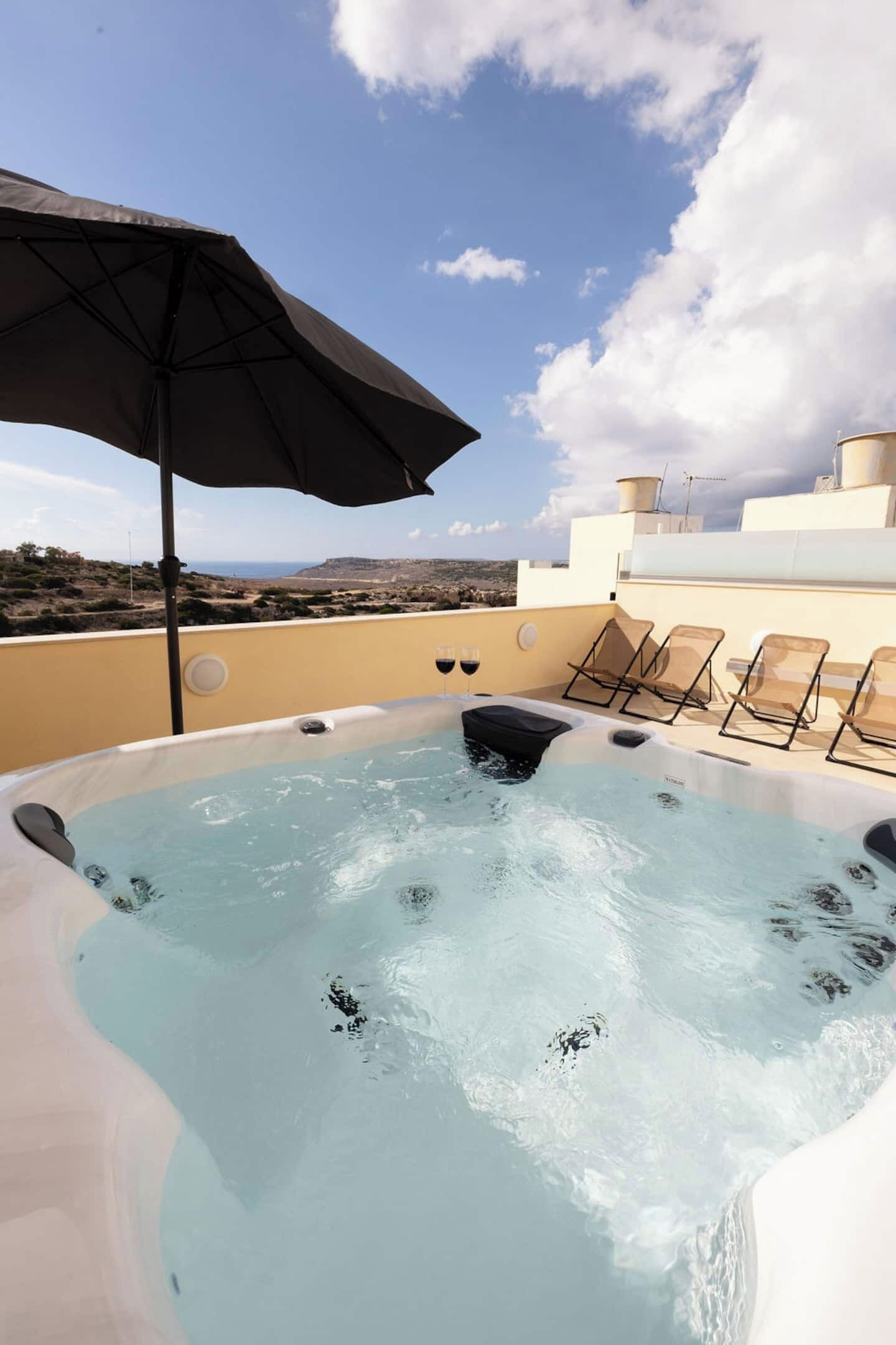 A rooftop hot tub with lounge chairs and an umbrella, overlooking a scenic landscape.