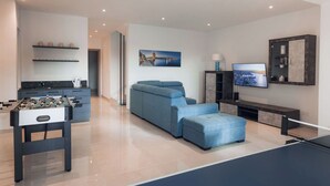 A modern living room with a foosball table, a blue sofa, and a television.