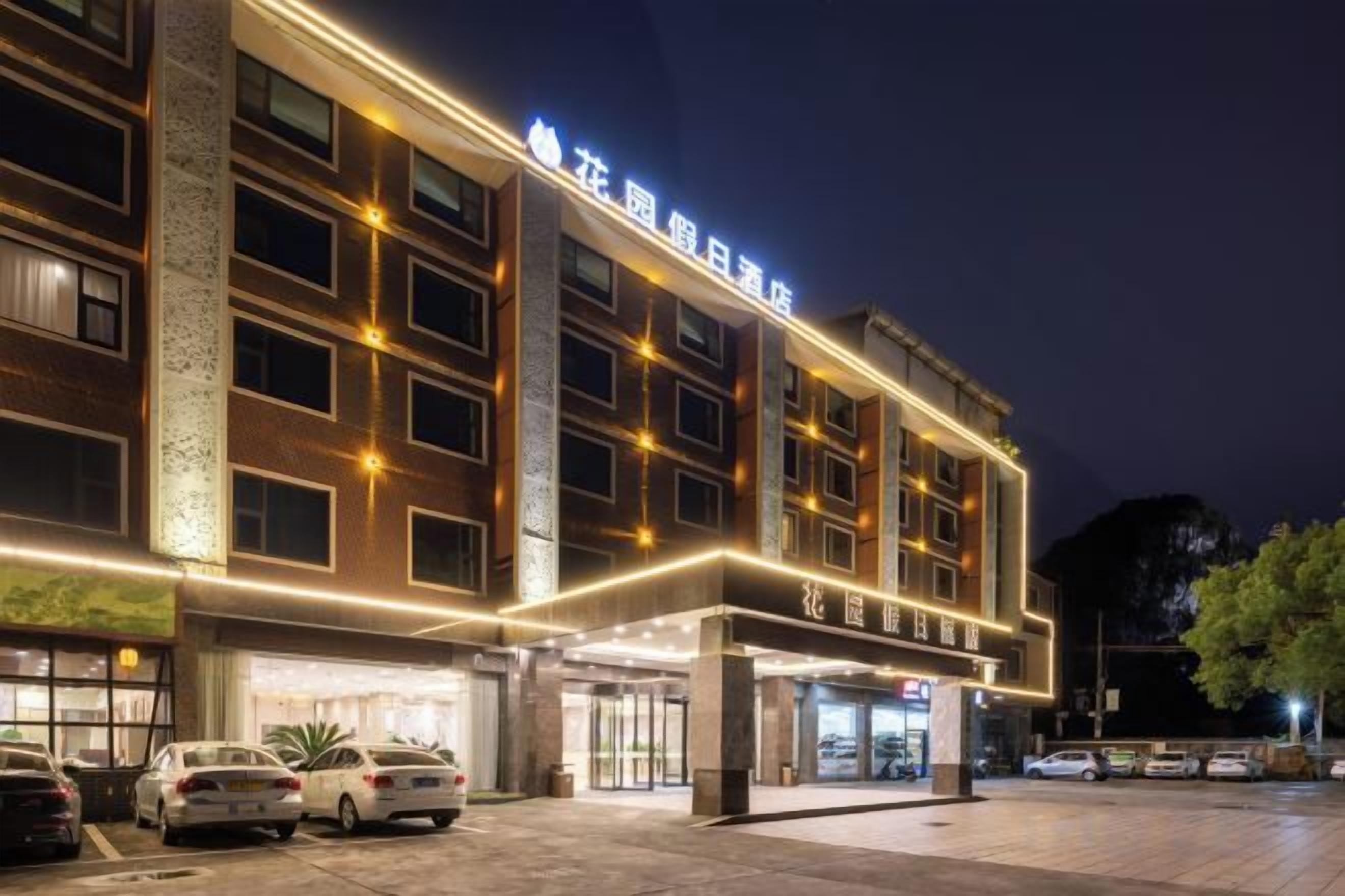 Een meerhoog hotel met een opvallende ingang, een parkeerplaats en een goed verlichte gevel.