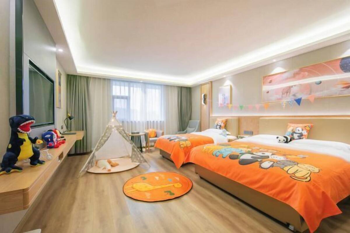 A hotel room with two beds, a play area with toys, a tent, and a large window.