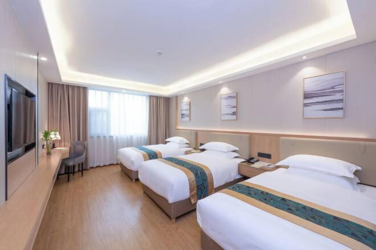 A hotel room with three beds, a TV, a desk, and a window with curtains.