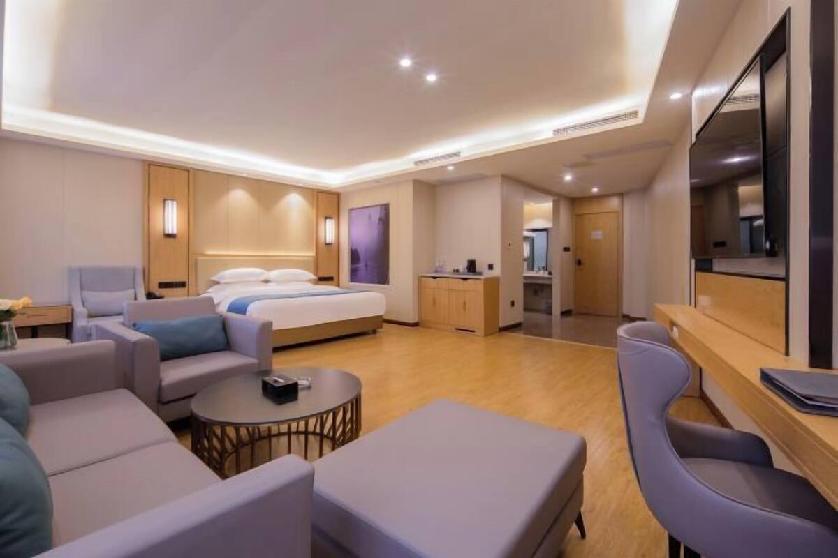 A modern hotel room with a bed, seating area, kitchenette, and a TV.