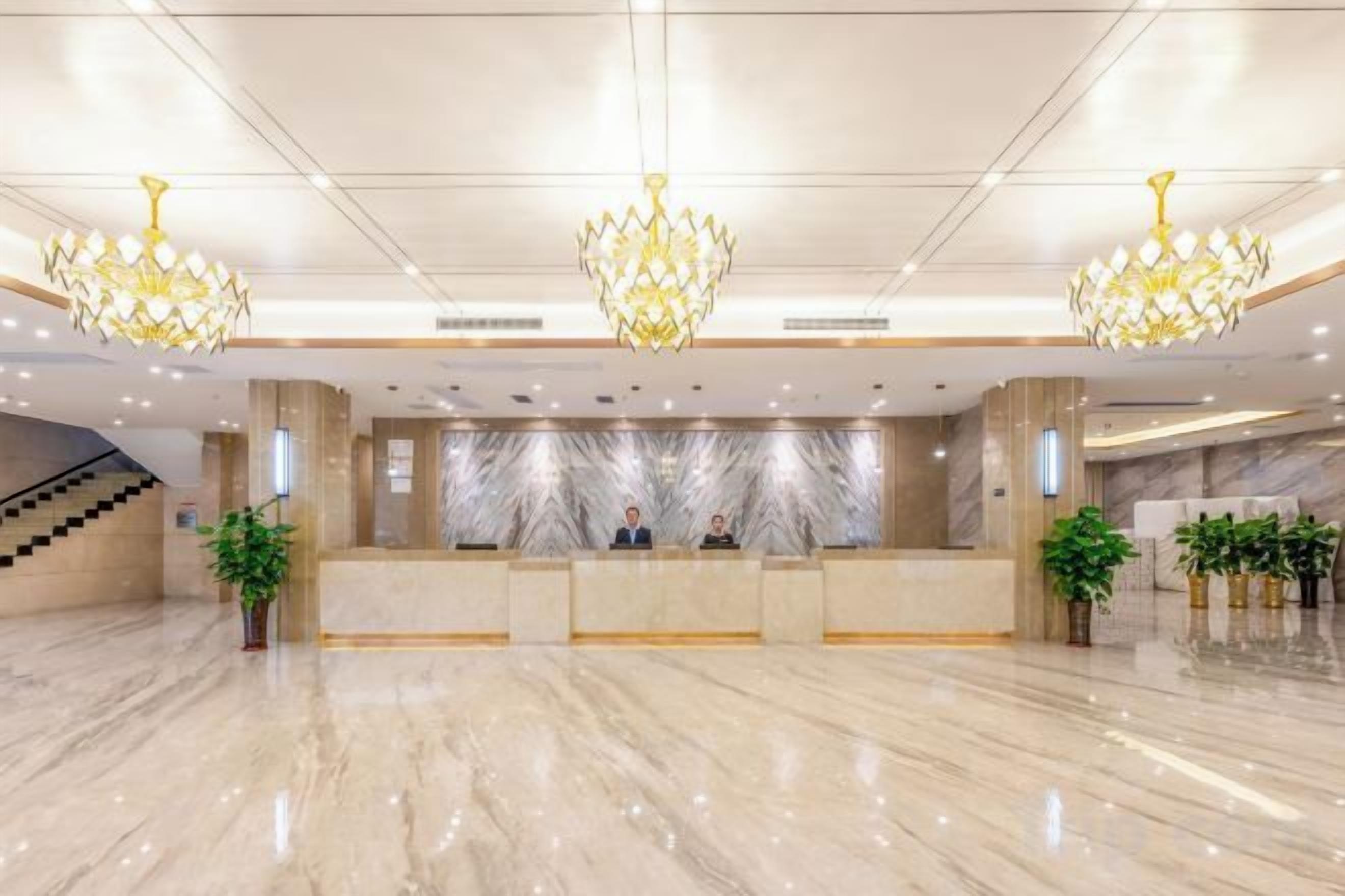 Zona de recepción de un hotel con suelo de mármol, un mostrador de recepción y tres candelabros.