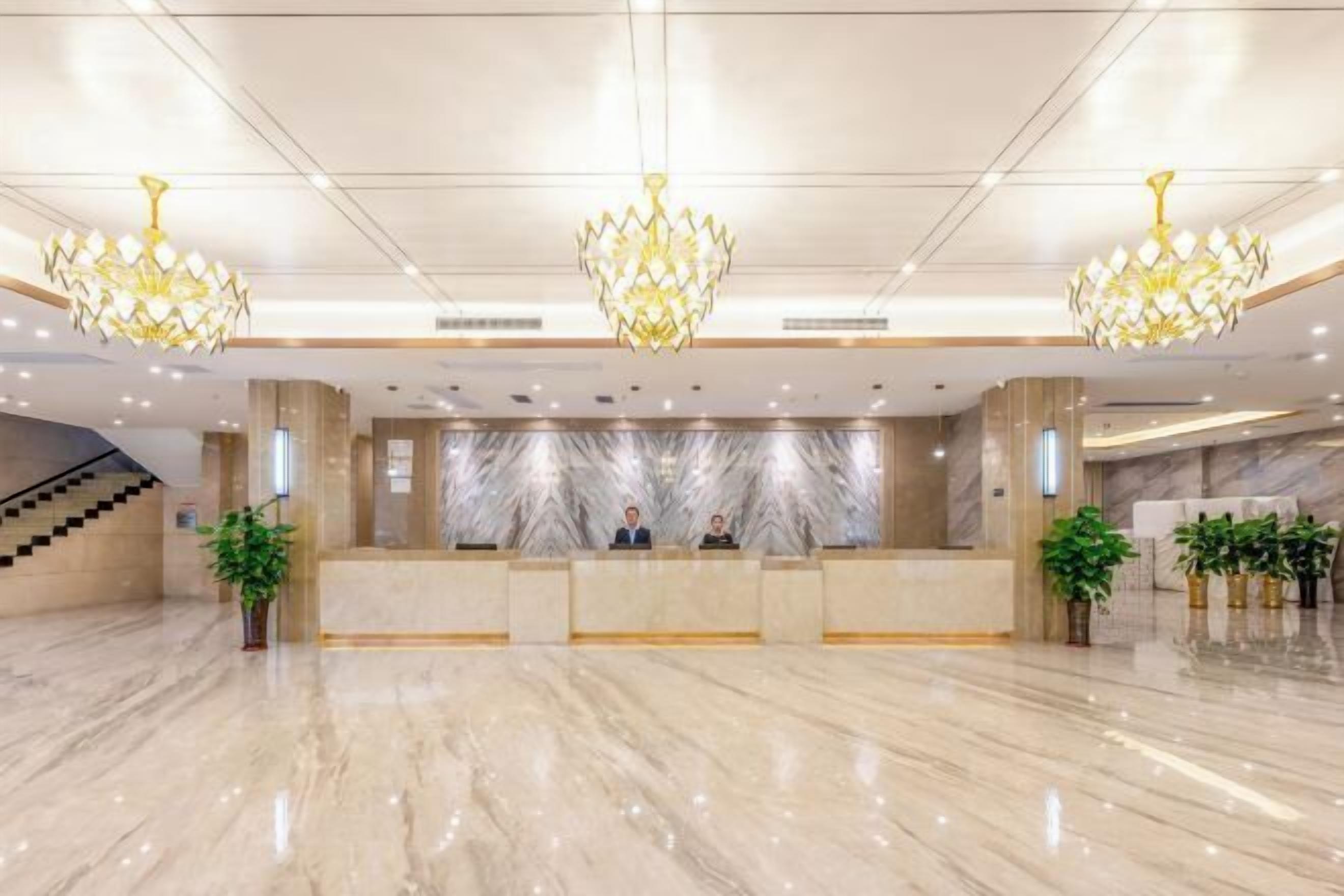 A spacious lobby with a marble floor, a reception desk, and three chandeliers.