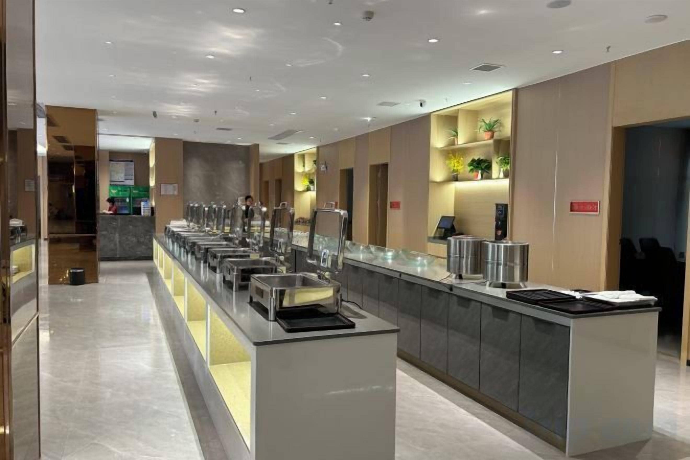 Een moderne hotelkeuken met een lange toonbank, meerdere voedseldispensers en een zithoek met stoelen.