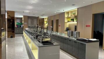 Een moderne hotelkeuken met een lange toonbank, meerdere voedseldispensers en een zithoek met stoelen.