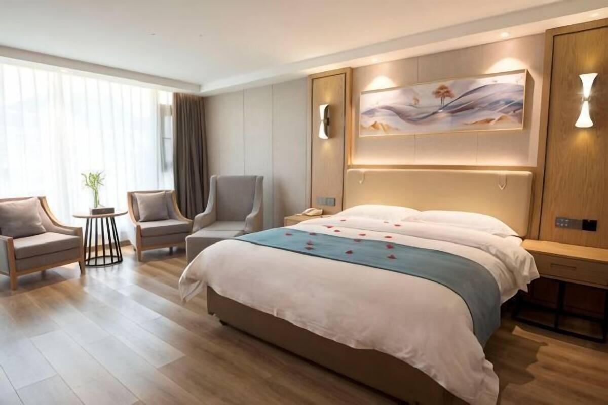 A hotel room with a large bed, two armchairs, a small table with a plant, and a painting on the wall.