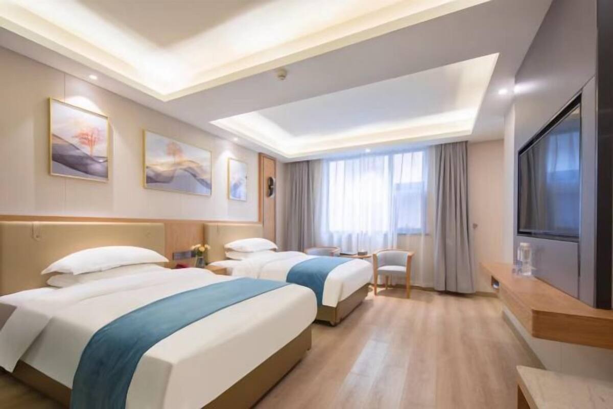 A hotel room with two beds, a TV, a desk, and artwork on the walls.