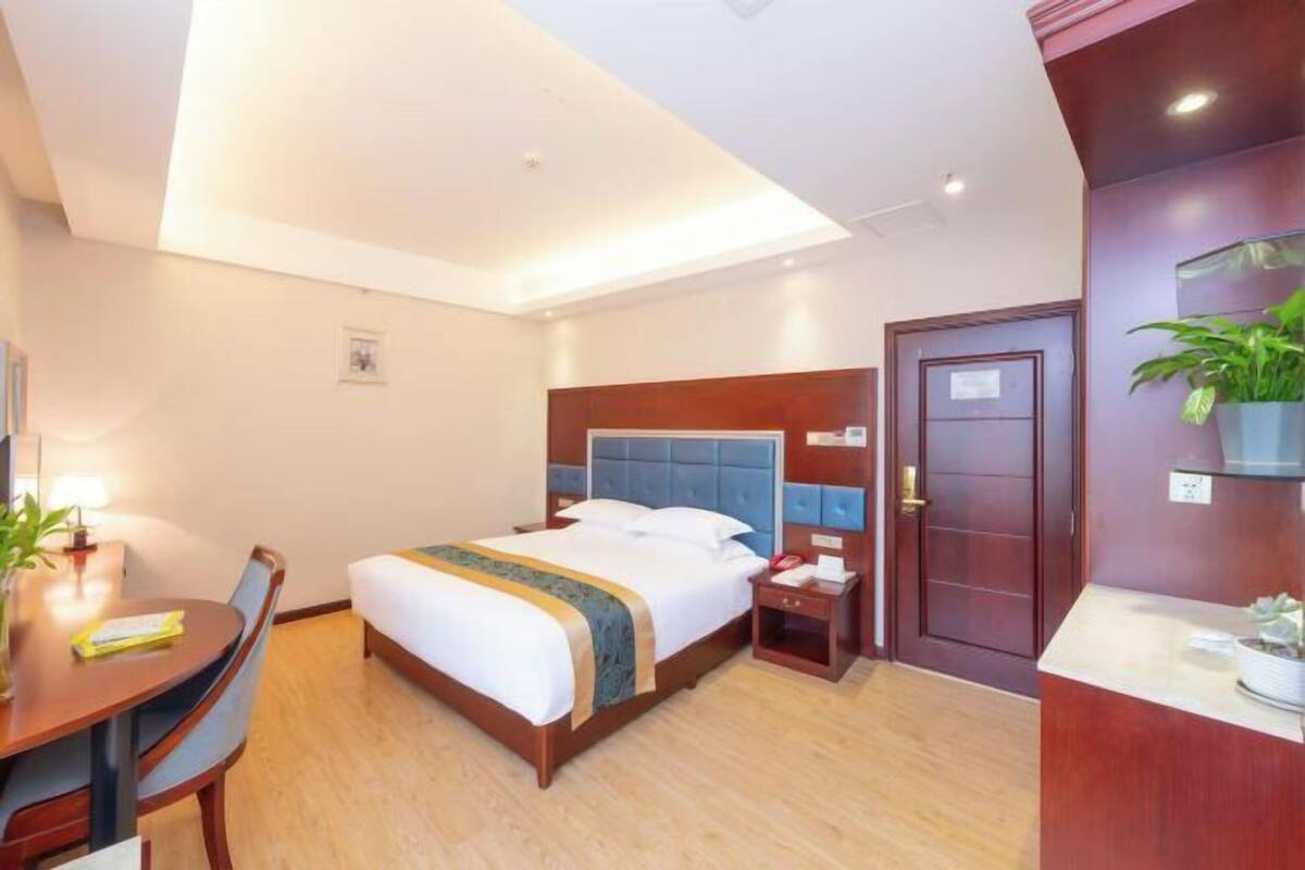 A hotel room with a bed, bedside table, chair, desk, and a door.