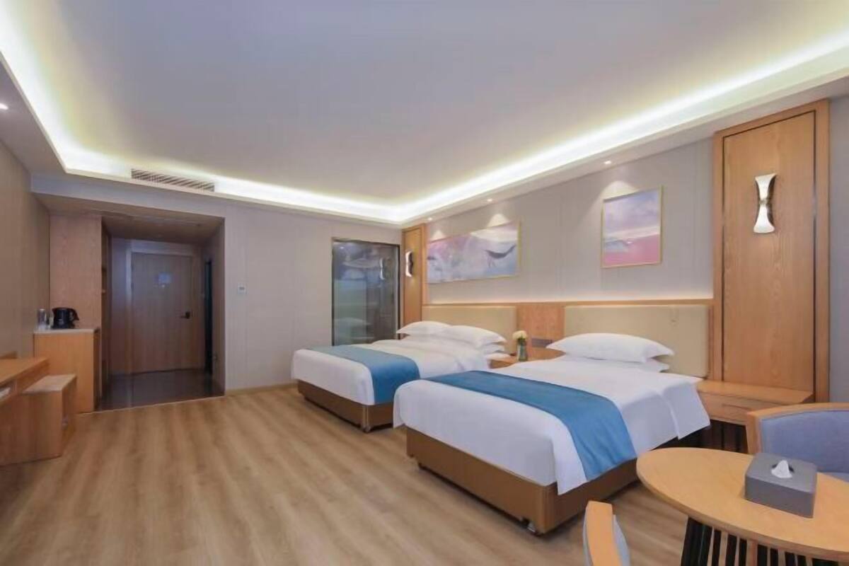 A hotel room with two beds, a wooden desk, a round table, and a door leading to another room.