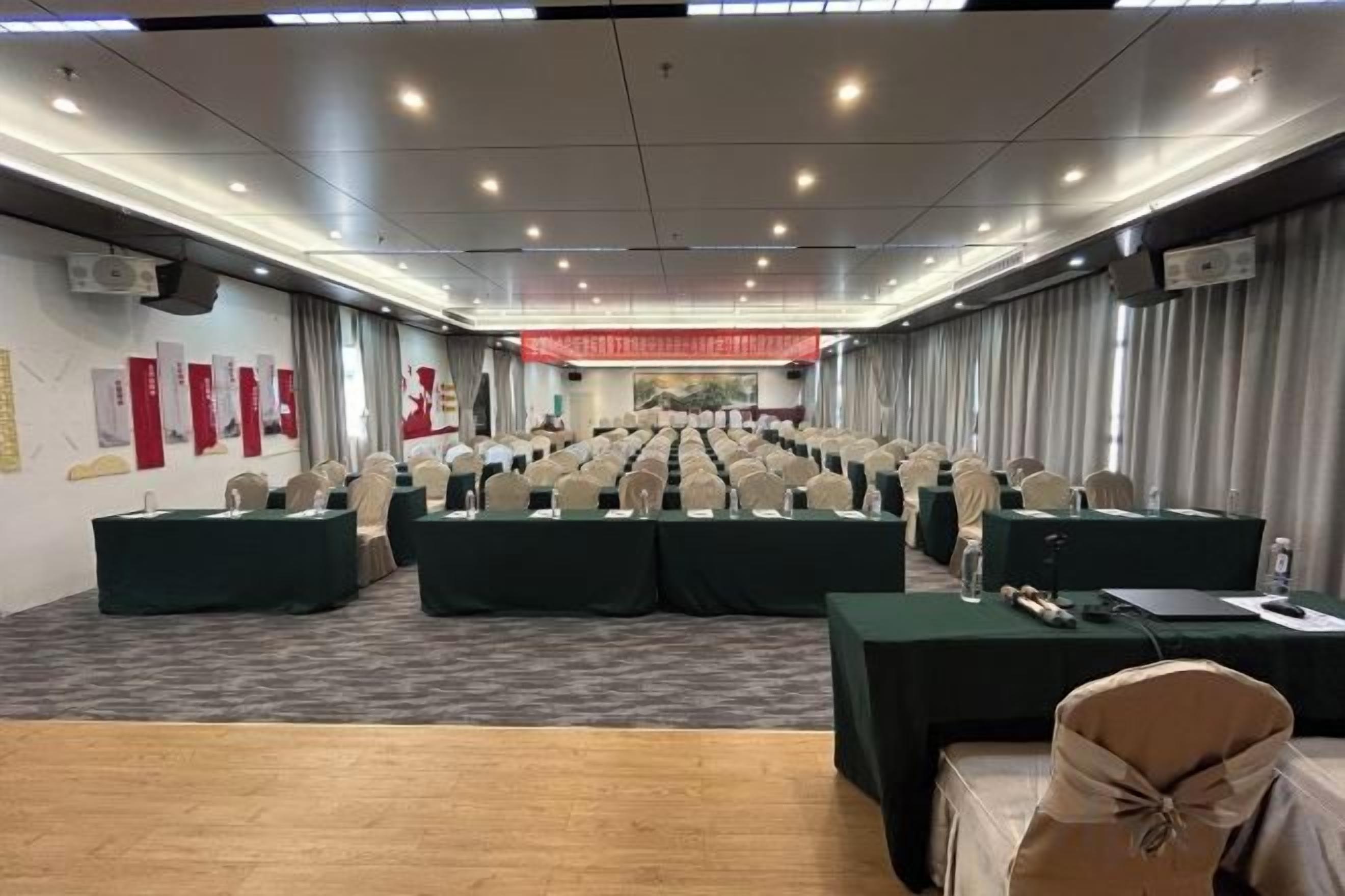 Un salón de conferencias con filas de sillas, mesas y un escenario al frente.