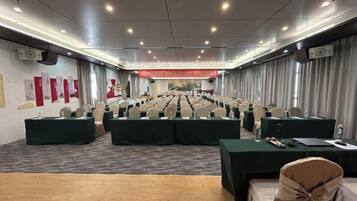Un salón de conferencias con filas de sillas, mesas y un escenario al frente.
