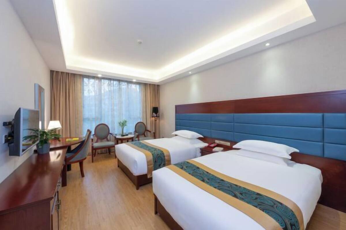 A hotel room with two beds, a desk, a chair, a TV, and a window with curtains.