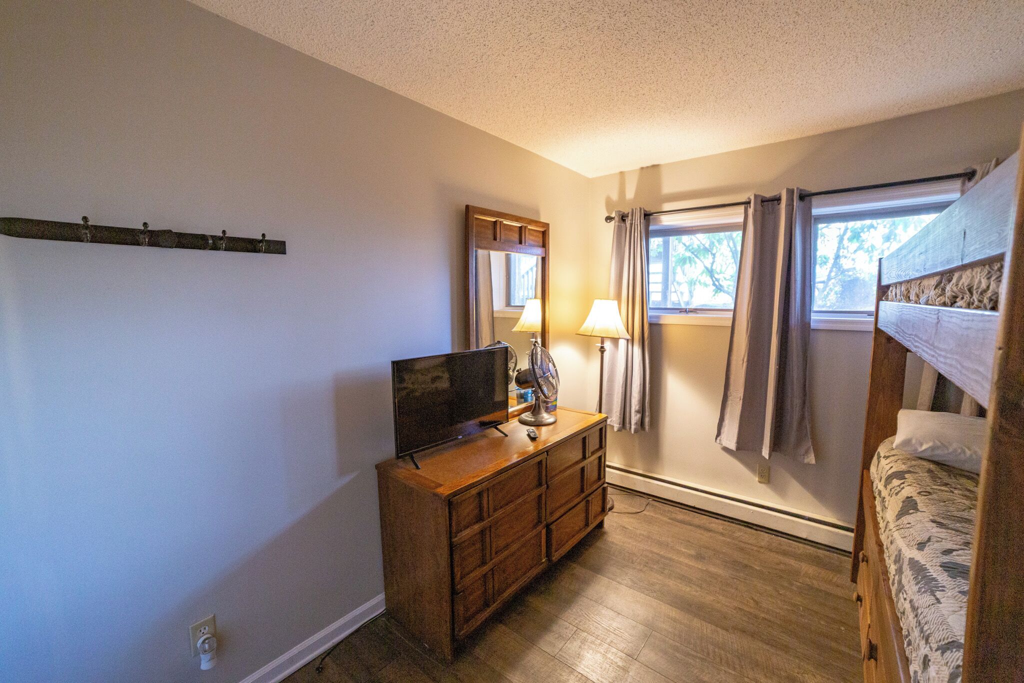 A bedroom with a wooden dresser, a television, a window with curtains, and a bunk bed.