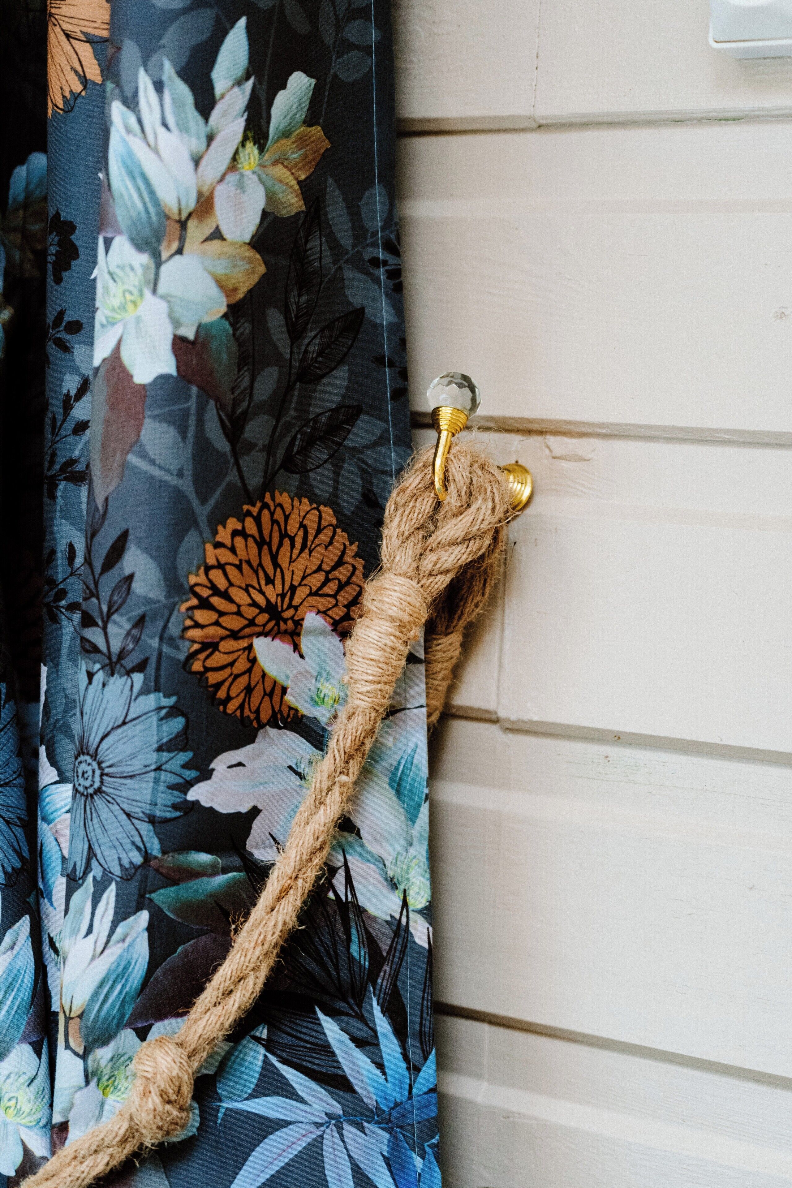 Un rideau orné d’un motif floral et une corde attachée à un crochet en laiton.