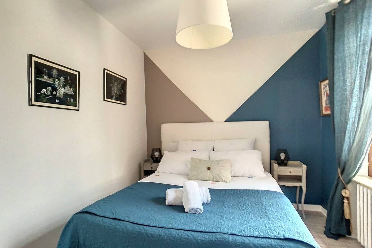 Une chambre à coucher avec un lit, deux tables de chevet, un luminaire suspendu et deux tableaux encadrés accrochés au mur.