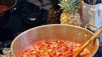 A large pot on a stove with a wooden spoon inside, surrounded by kitchen utensils and a pineapple.
