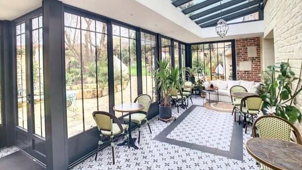 A sunlit patio with large windows, wicker furniture, and a potted plant. - Les Glycines de Monchy (Monchy-Humieres)