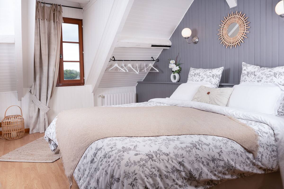 Une chambre avec un lit, un portant à vêtements, une fenêtre et un miroir fixé au mur.