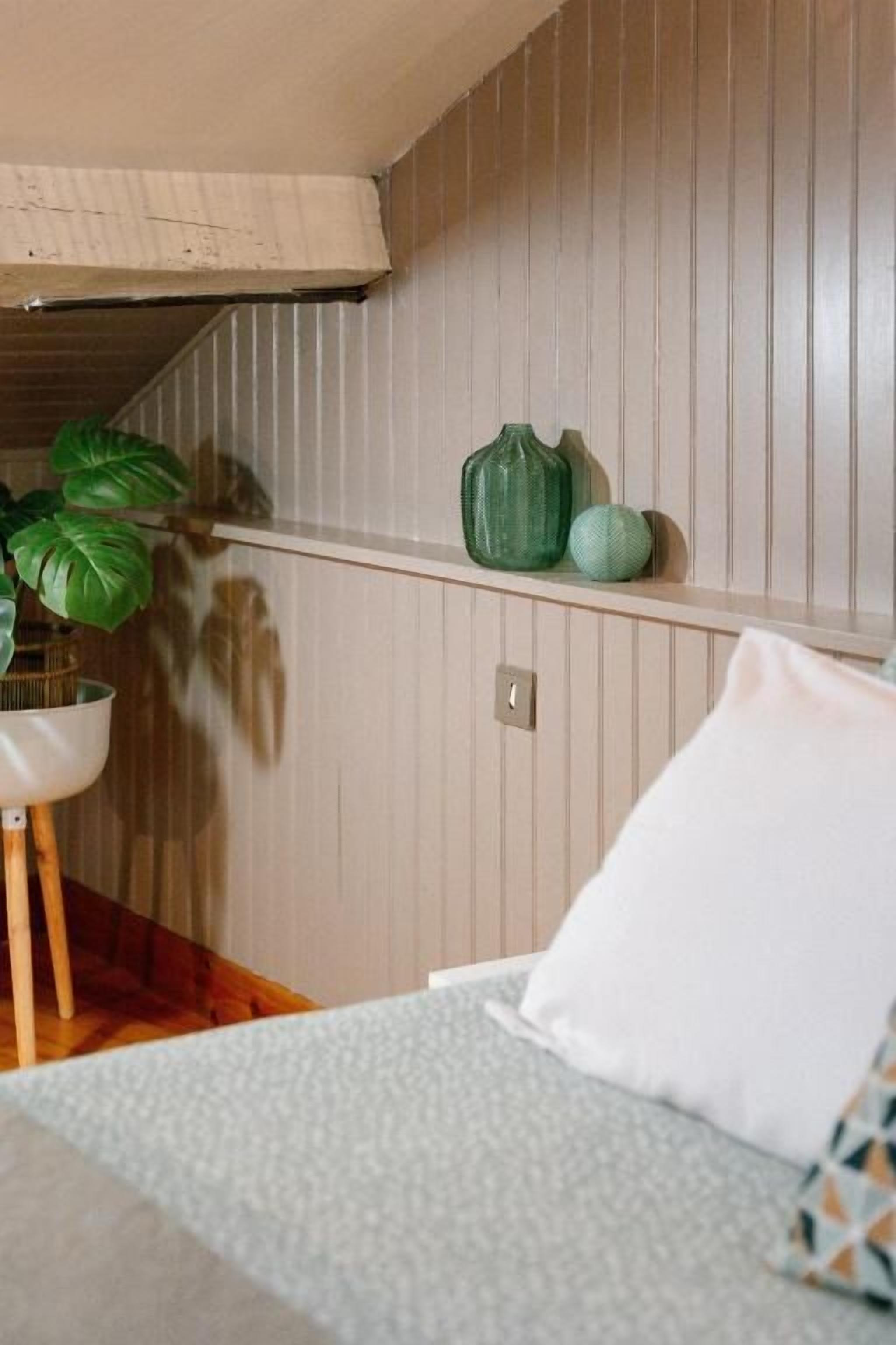 Un dormitorio con una cama, una mesita de noche con una planta y una estantería con adornos.