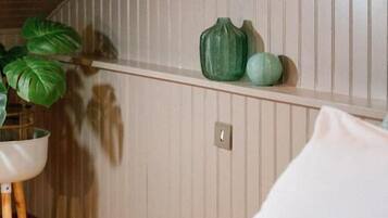 Un dormitorio con una cama, una mesita de noche con una planta y una estantería con adornos.