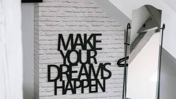 Une pièce avec un mur en briques blanches, une citation inspirante, un grand miroir et une moquette bleue.