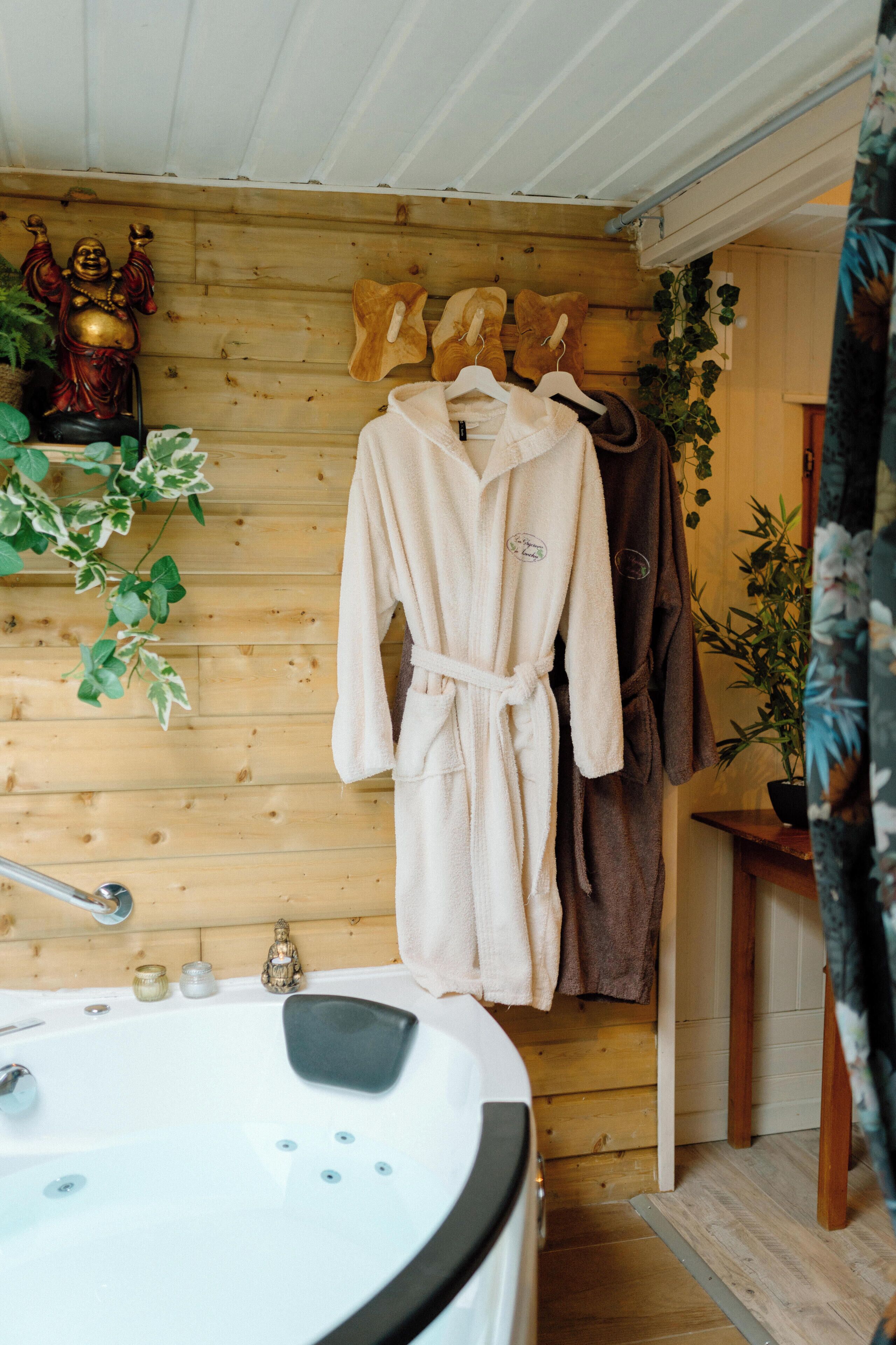 A wooden interior with a sauna, a bathtub, and a robe rack with robes.