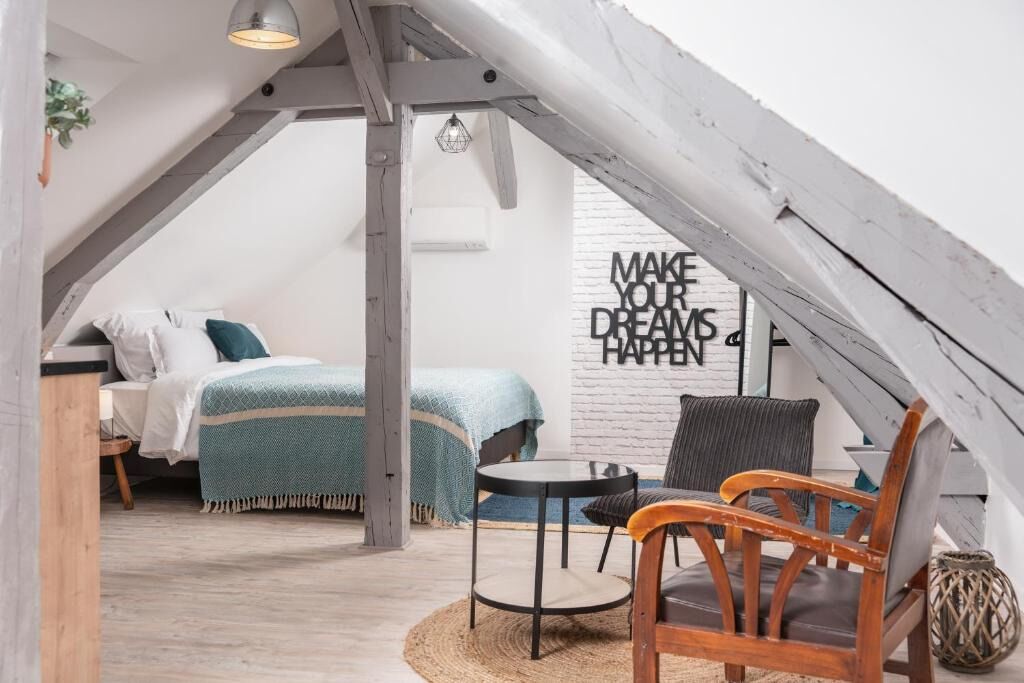 A cozy attic bedroom with a bed, a chair, a small table, and a wall with motivational text.