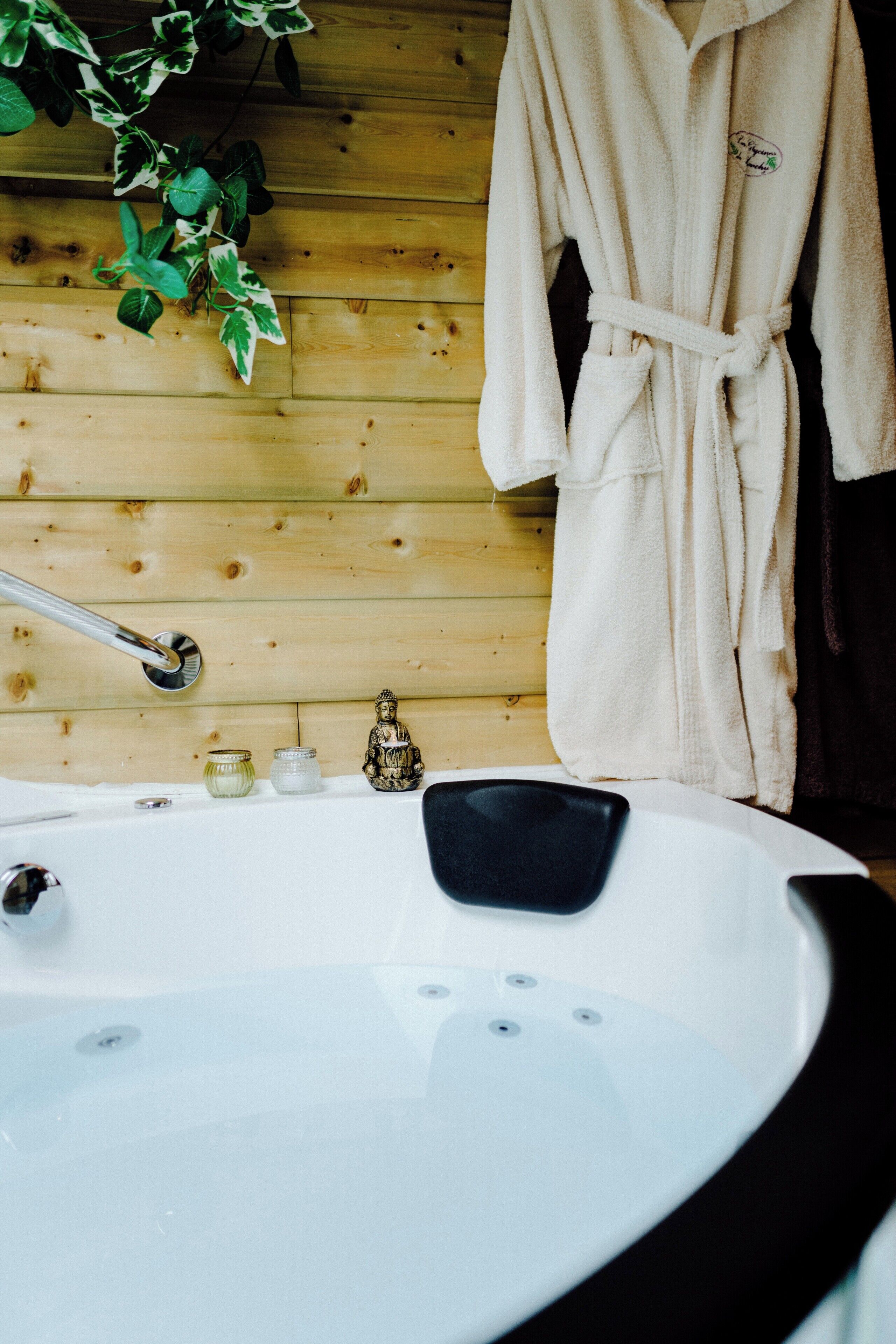 A wooden cabin interior with a white bathtub, a hanging bathrobe, and a Buddha statue.
