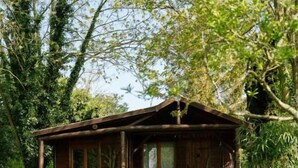 A wooden cabin with a porch, surrounded by lush greenery and a stone pathway. - Les Glycines de Monchy (Monchy-Humieres)